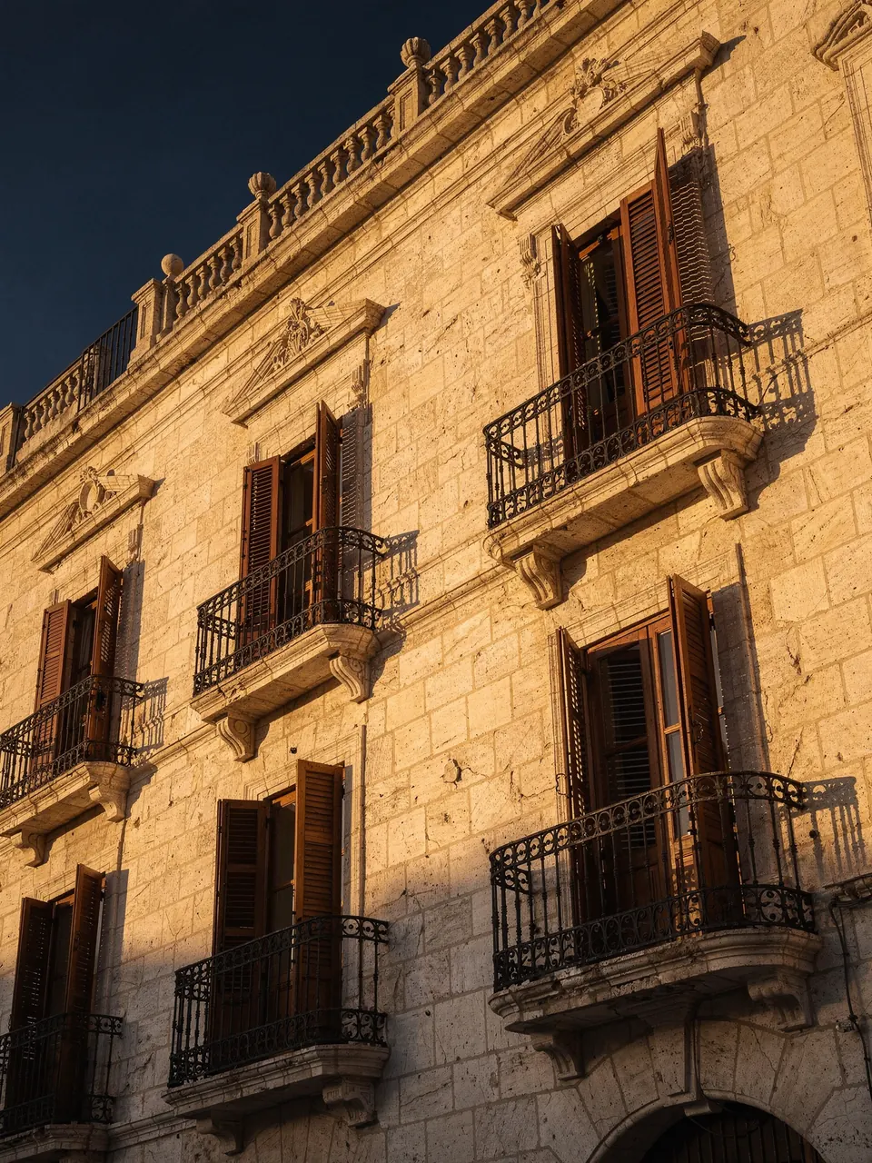 Fachada clásica de piedra restaurada con balcones de forja, iluminada por la luz del atardecer